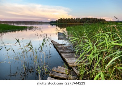 Sunset view of the lake with an old broken wooden pier, thickets of reeds and reflection on the surface of the water - Powered by Shutterstock