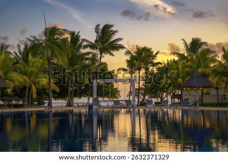 Sunset view of a luxury resort pool with palm trees, lounge chairs, and beach access in Mauritius.