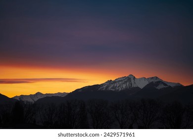 a sunset view of a mountain range with trees in the foreground and a red and yellow sky in the background. . 