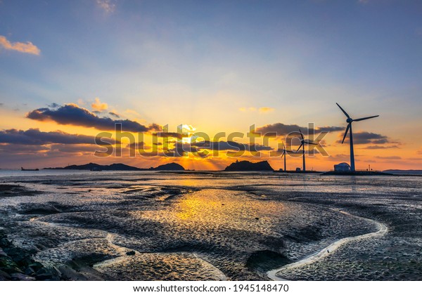 Sunset view of mud flat at Tando Port of Daebudo\
Island with the background of wind power generators near Ansan-si,\
South Korea \
