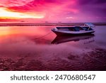 Sunset view at Nunsui Beach features a traditional wooden boat against a backdrop of reddish-purple hues. The sky