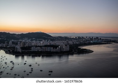 Sunset View Over Guanabara Bay From Sugarloaf Mountain In Urca Towards City Of Rio De Janeiro With Boats In Bay & Mountains In Background With A Warm Summer Sky Overhead In Rio, Brazil, South America