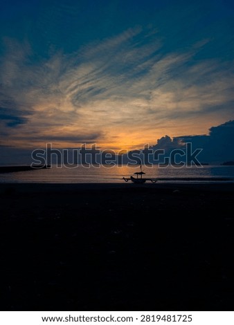 A sunset view partially covered by clouds on the beach with a silhouette of a fishing boat and a breakwater.
