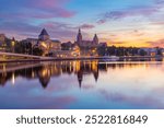 Sunset view of the Szczecin riverfront along the Oder River in Poland, featuring the illuminated Waly Chrobrego buildings and their reflection in the calm water