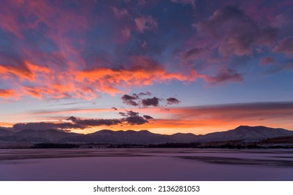 Sunset Winter Mountain Lake - A panoramic view of colorful sunset clouds hovering over a frozen mountain lake. Bear Creek Lake, Denver-Lakewood-Morrison, Colorado, USA.