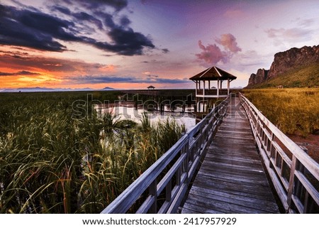 Sunset at Wooden path with pavilion on the marshes near the rock mountain.