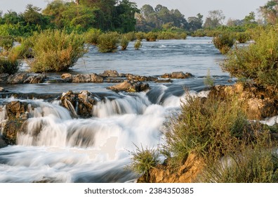 At sunset.Sunlight shining on rocks,next to blurred movement of water,rushing by,at the main waterfalls and rapids of Don Khon island.