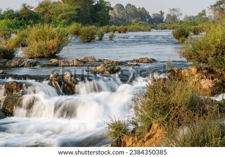 At sunset.Sunlight shining on rocks,next to blurred movement of water,rushing by,at the main waterfalls and rapids of Don Khon island.