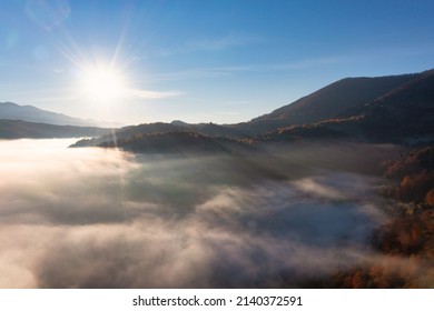 Sunsetting light shining brightly on pink and purple sky above thick layer of white fog covering mountainous canyon panorama view