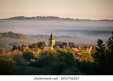 Sunshine on the village and church of Nabirat in the Dordogne region of France with early morning mist over the distant woodland - Powered by Shutterstock