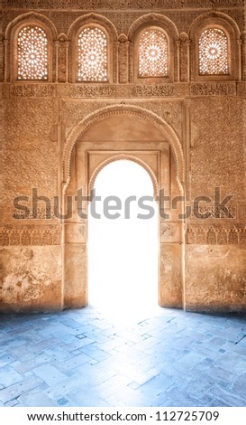 Sunshine through door to Granada palace. Sunlight on blue floor. Stone wall and windows in arabesque design. Ornate pattern of building in arabic style. Famous tourist destination in Spain, Europe.