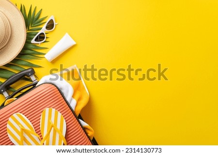 Sun-soaked dreams. Top view setup displaying a suitcase, beach essentials, glasses, sunhat, sunscreen, flip-flops, towel, palm leaf on vibrant yellow backdrop. Empty space provided for text or adverts
