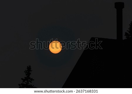 Sunspots on a Setting Sun in focus, and Silhouette of a House, Chimney and Trees in the Foreground