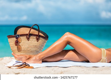 Suntan beach vacation woman legs lying on sand towel relaxing on summer holidays. Body care sexy toned leg for cellulite or hair removal laser treatment concept.