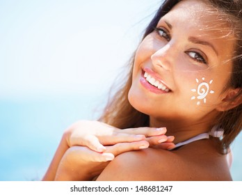 Suntan Lotion Woman Applying Sunscreen Solar Cream. Beautiful happy cute Girl applying Sun Tan Cream on her Face with ocean in background. Sun Tanning. Skin Protection