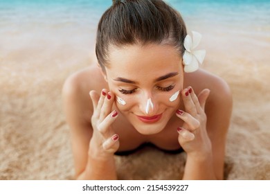 Suntan lotion woman applying sunscreen solar cream. Beautiful happy cute woman  applying suntan cream from a plastic container to her nose with ocean in background.