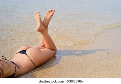 Suntan and vacation. Close up of sexy young woman in bikini laying on sand beach.