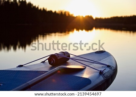 SUP board and surf board with paddle on blue water surface background close up. Surfing and SUP boarding equipment in sunset lights close-up. Outdoor water sports. Surfing lifestyle backgrounds.