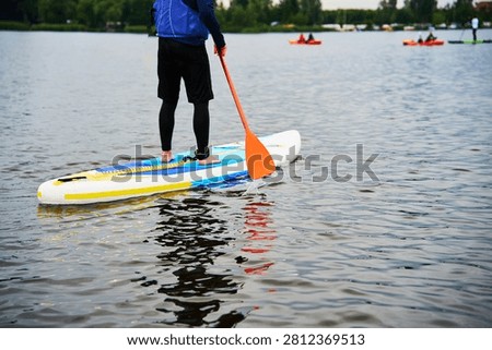 SUP boarder using a paddle on a wide river. Water sports recreation and fitness concept. Person standing on an inflatable board wearing a life vest while performing a stroke