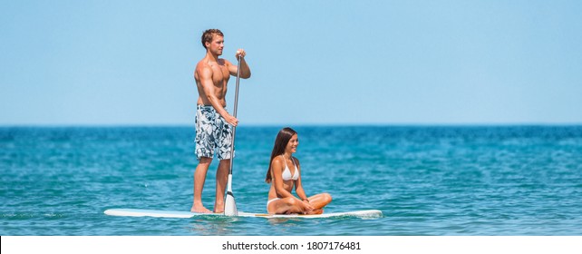 SUP Inflatable paddle board man athlete paddleboarding with woman on paddleboard. Fun summer watersport sport for couples on vacation. Panoramic banner.