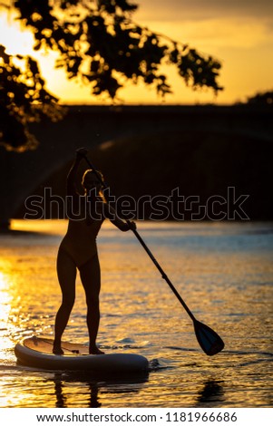 SUP Stand up paddle board concept - Pretty, young woman paddle boarding on a lovely lake in warm late afternoon sunset light