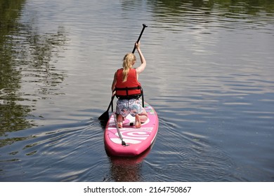 Sup surfing, blonde girl in life vest with paddle sailing on a board in river. Stand up paddle boarding in summer