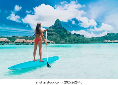 SUP Tahiti paddleboard woman standing on stand-up board paddling over turquoise ocean at luxury beach resort hotel on Bora Bora island, French Polynesia.