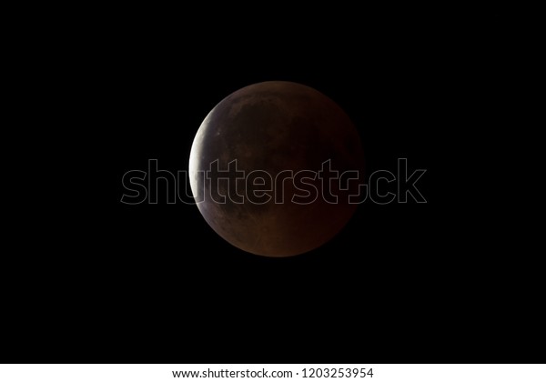Super Bloody Moon, full eclipse end phase against\
black sky background, Earth\'s shadow starting to move out from the\
Moon surface