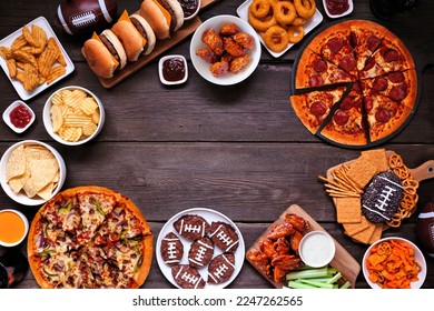 Super Bowl or football theme food frame. Pizza, hamburgers, wings, snacks and sides. Above view on a dark wood background.