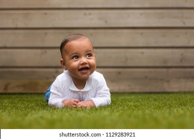 Super cute six months old little baby girl model laughing and lying on belly in the grass