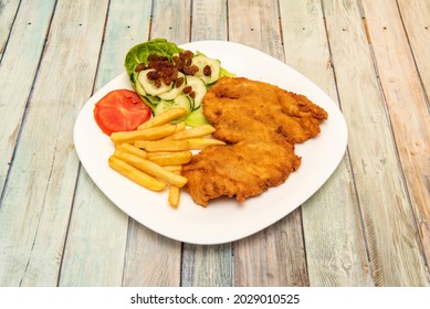 Super escalope of chicken breast breaded and fried in olive oil with a garnish of cucumbers with raisins with fried potatoes and tomato