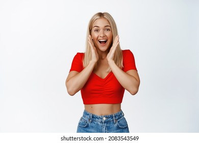 Super Excited Blond Girl Screams, Smiles And Looks Surprised, Stands Agaisnt White Background In Summer Outfit