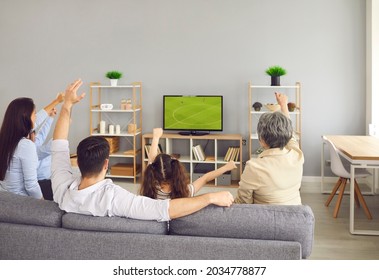 Super Excited And Happy Big Family Team Watch Football Match Together On The Couch At Home. Rear View Of Young And Older Family Members Sitting With Their Arms Raised While Watching A Match On TV.