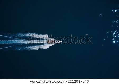 super fast open big boat with people moving fast on dark blue water making a white trail behind the boat.