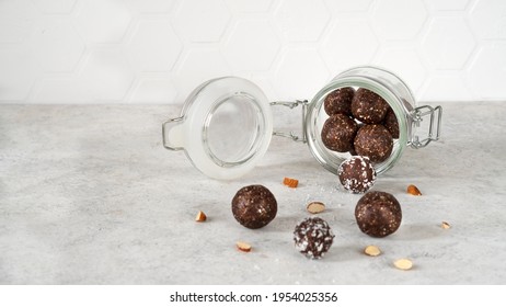 Super food energy balls. Healthy protein balls with nuts, dates, peanut butter, cocoa powder, coconut flakes, oats in glass jar. Homemade truffles. Vegan raw food snack. Side view. Copy space.