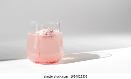 Super food. Glass of natural strawberry collagen protein powder in glass of water for skin regeneration. Trendy food additives. White background with sunlight and deep shadow of glass. Hard sunlight.
