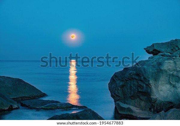 Super full blood moon and moon light over the\
sea. Full red moon with reflection in water with details of the\
lunar surface.