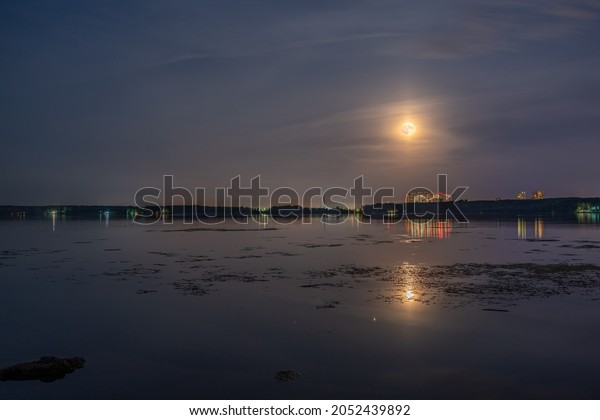 Super full blood moon and moon light over the\
nigt lake. Full red moon with reflection in water with details of\
the lunar surface.