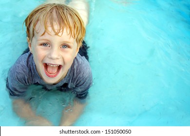 A Super Happy Child Is Laying In A Small Wading Pool, Looking Up At The Camera And Smiling.  Empty Space Off To The Side For Text / Copy Space.