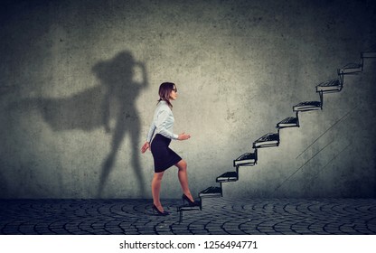 Super hero business woman stepping up on stairs climbing to success on gray wall background