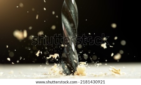 Super macro shot of steel drill with wood chippings flying off. Sawdust flies off a spinning drill boring a hole into a wooden board.