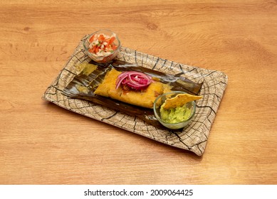 Super Mexican tamale stuffed with cochinita pibil meat with guacamole with tortilla chips and pico de gallo on a plate similar to a wooden log