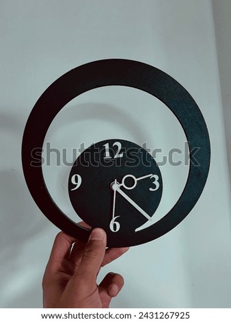 Super minimalist black colour wall clock held in a hand on a white background with hands and numbers in white colour.