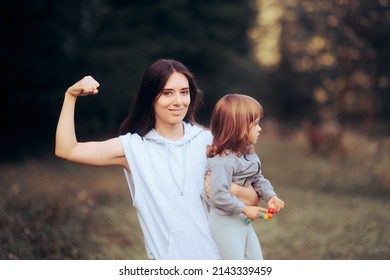 
Super Mom Holding Her Toddler Daughter Flexing Muscles. Active Mother Wearing Sports Clothes Exercising And Babysitting
