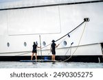 Super yacht crew, two deckhands, male and female cleaning the side of a white mega at dock in English Harbour, a famous caribbean island of Antigua know for yacht season