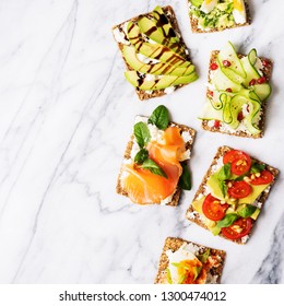 Superfood protein toast with delicious toppings on top: avocado, salmon, eggs, vegetables, tomatoes, herbs, pine nut, sunflower seeds and cream cheese on marble. Healthy diet concept with copy space.
