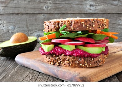 Superfood Sandwich With Beet Hummus, Avocado, Vegetables And Greens, On Whole Grain Bread Against A Wooden Background