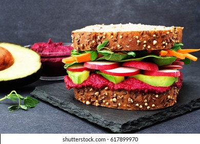 Superfood Sandwich With Beet Hummus, Avocado, Vegetables And Greens, On Whole Grain Bread Against A Slate Background