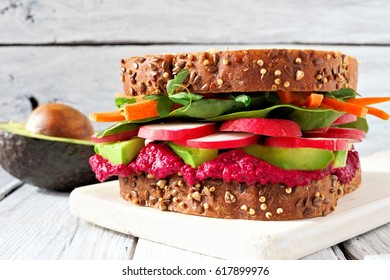 Superfood Sandwich With Beet Hummus, Avocado, Vegetables And Greens, On Whole Grain Bread Against A White Wood Background