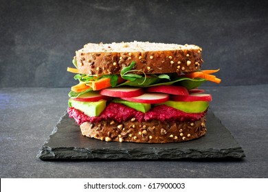 Superfood Sandwich With Beet Hummus, Avocado, Vegetables And Greens, On Whole Grain Bread Against A Slate Background